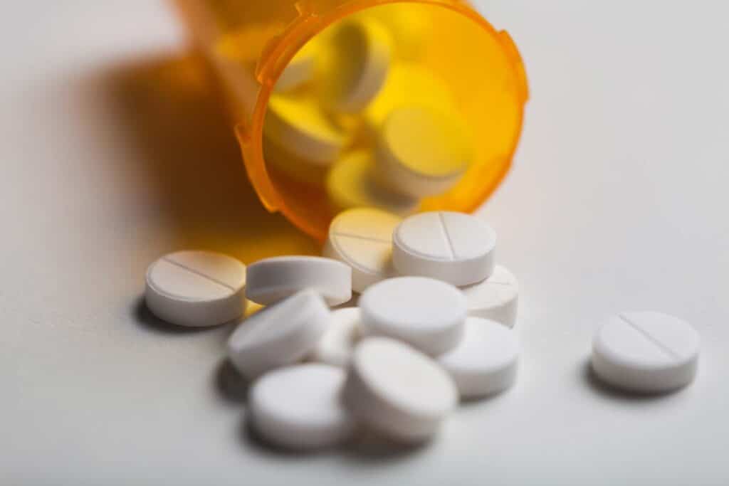 Close up of white opiate tablets spilling out of a pill bottle, representing the Johnson & Johnson settlement.