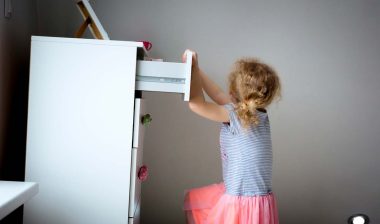 A piece of furniture tipping over as a young girl attempts to climb it, representing the furniture restraint kits.