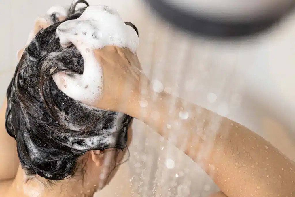 Woman lathering her hair with shampoo in the shower, representing the Neutrogena shampoo class action.