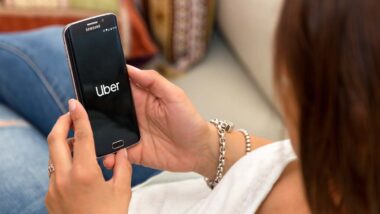 Back view of a woman using the Uber app on her smartphone, representing the Uber lawsuits.