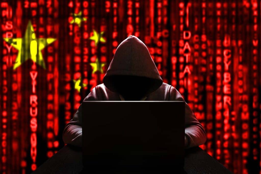 A hooded hacker using a computer with a Chinese flag in the background, representing Chinese hackers targeting United States systems.