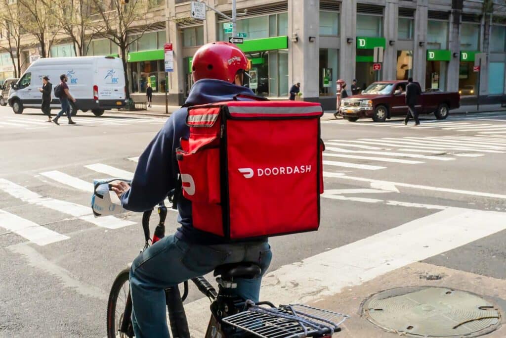 A Door Dash worker delivering on a bike with a Door Dash bag, representing the DoorDash class action.