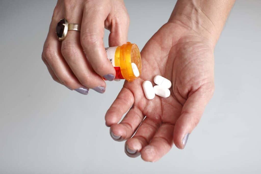Pain pills being poured from a pill bottle into hands, representing the Publicis opioid settlement.
