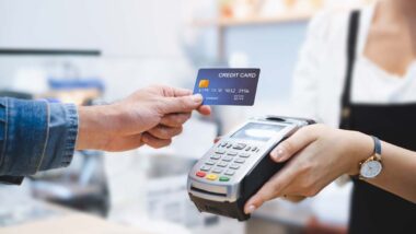 Close up of a man using a credit card on a POS machine, representing credit card late fees.