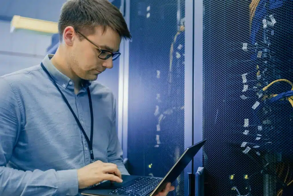 A male IT worker working on his laptop in a server room, representing the Wright & Filippis data breach settlement.