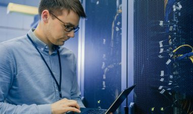 A male IT worker working on his laptop in a server room, representing the Wright & Filippis data breach settlement.