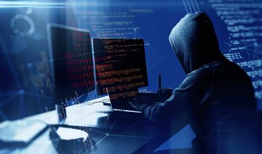 A hooded hacker using a computer, representing the Sovos Compliance data breach settlement.