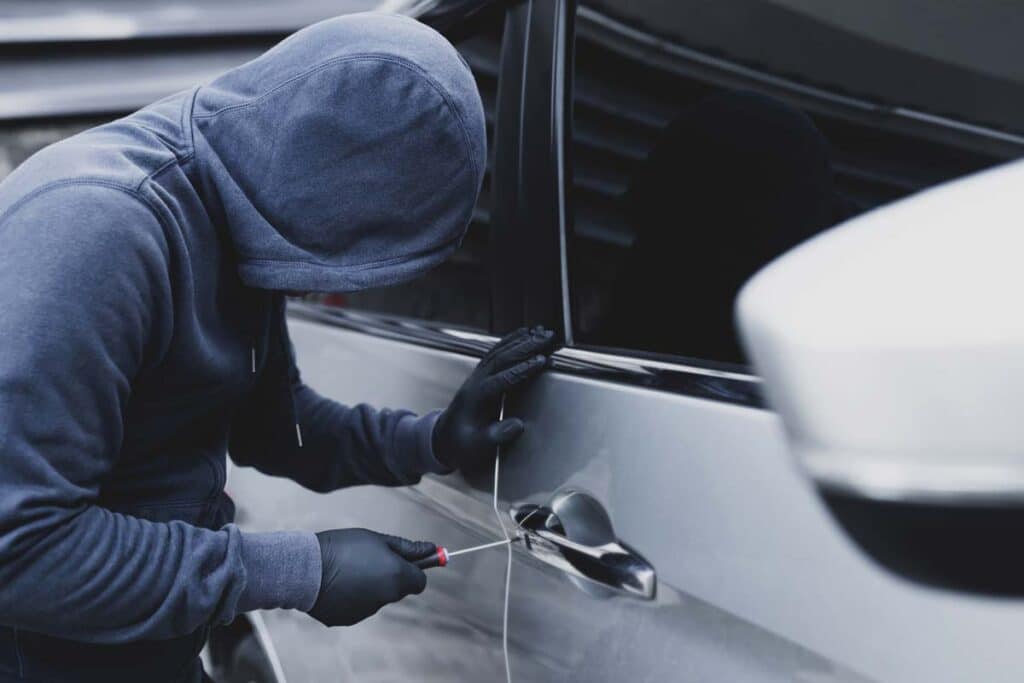 A hooded car thief using a screwdriver to break into a car, representing the Hyundai theft settlement.
