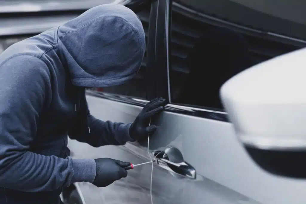 A hooded car thief using a screwdriver to break into a car, representing the Hyundai theft settlement.