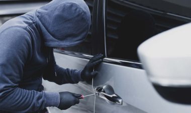 A hooded car thief using a screwdriver to break into a car, representing the Hyundai theft settlement.
