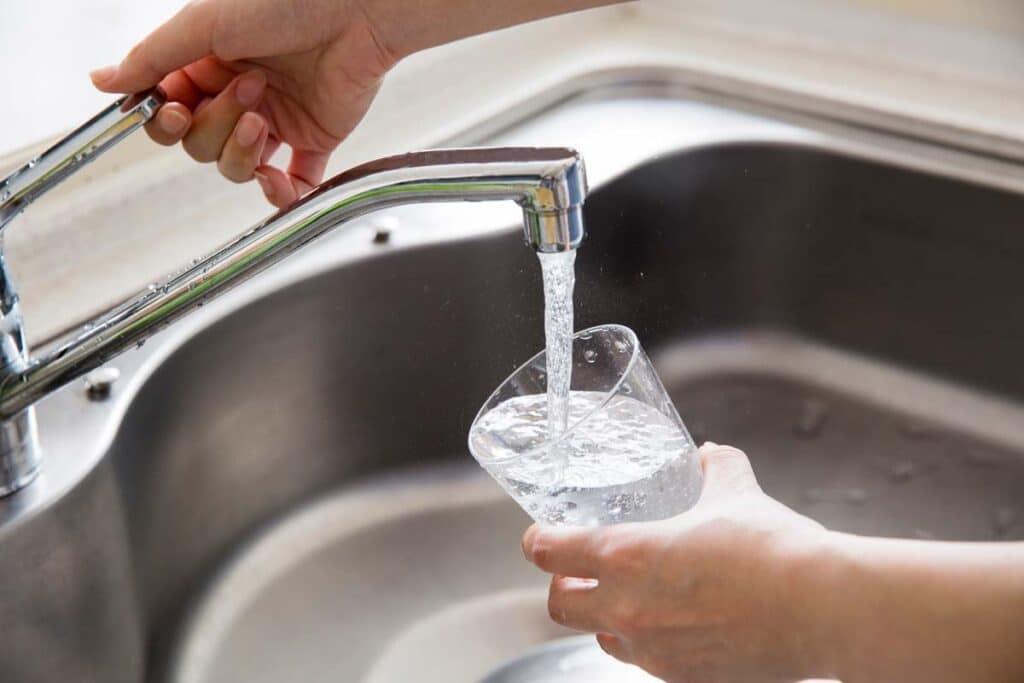 Closeup of a glass being filled with tap water from a faucet, representing the Kimberly-Clark drinking water PFAS class action.