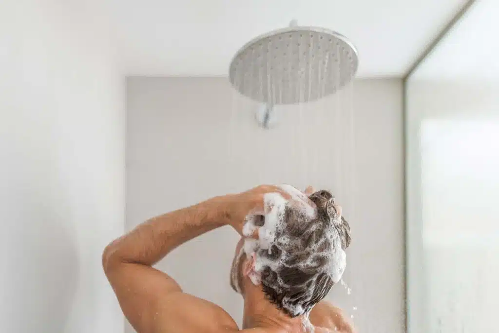 A man washing his hair with shampoo in the shower, representing Dr. Squatch shampoo class action lawsuit.