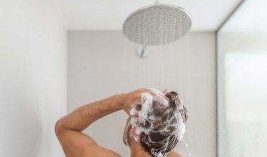 A man washing his hair with shampoo in the shower, representing Dr. Squatch shampoo class action lawsuit.
