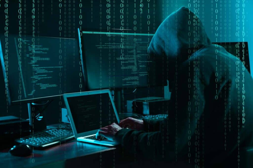 A hooded hacker typing on a laptop, representing the BioPlus data breach settlement.