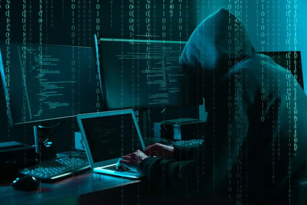 A hooded hacker typing on a laptop, representing the BioPlus data breach settlement. 