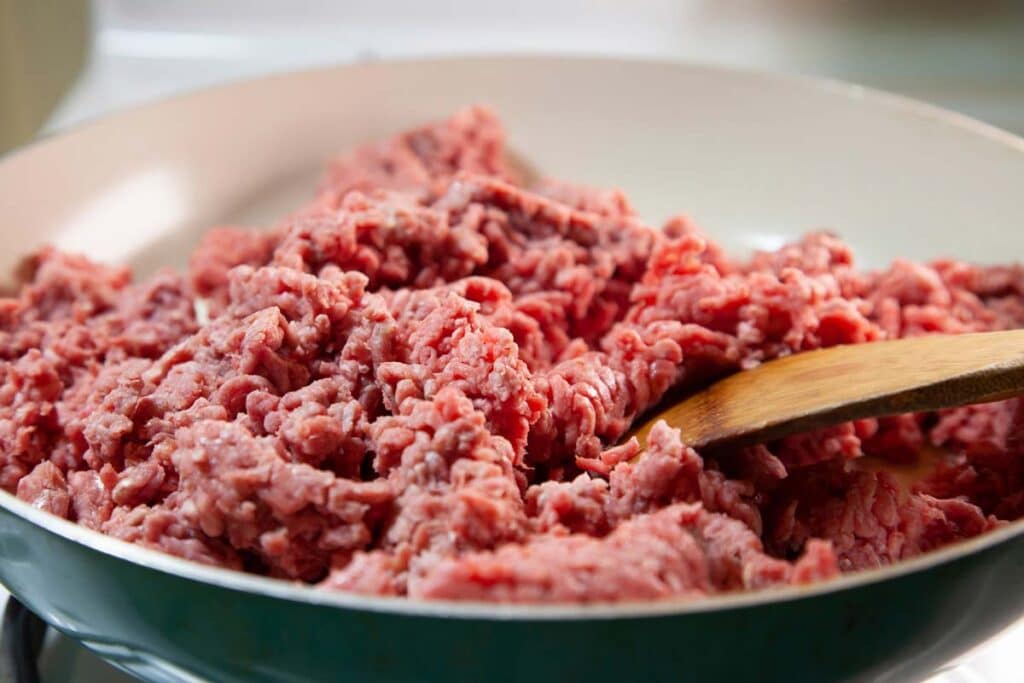 Close up of raw ground beef being cooked in a pan on a stove, representing the ground beef alert.