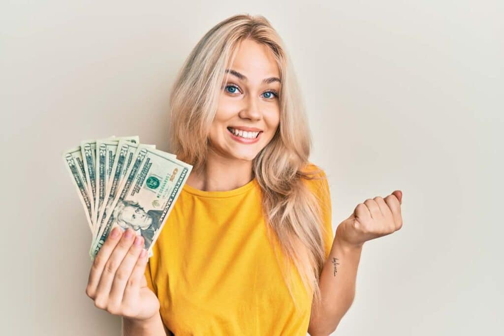 An excited woman holding cash, representing recent class action settlement payouts.