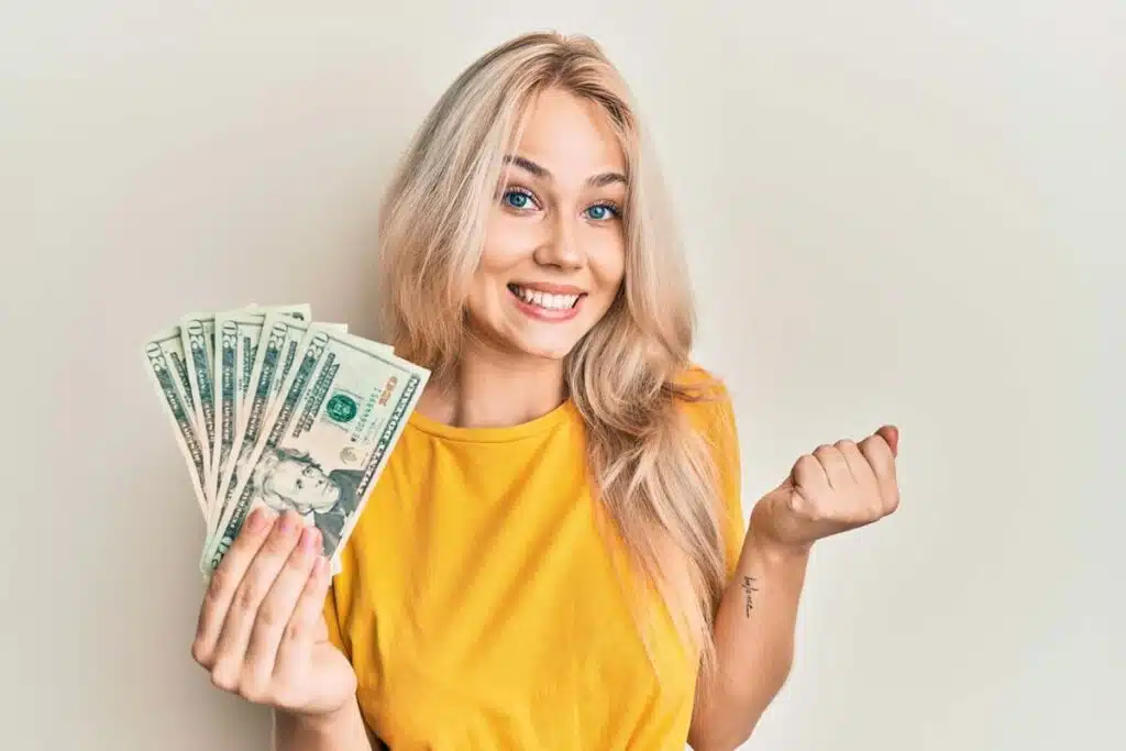An excited woman holding cash, representing recent class action settlement payouts.