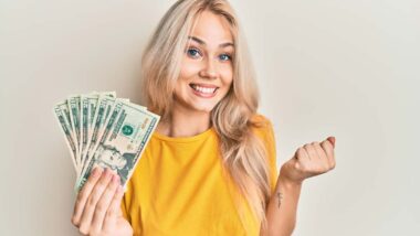 An excited woman holding cash, representing recent class action settlement payouts.