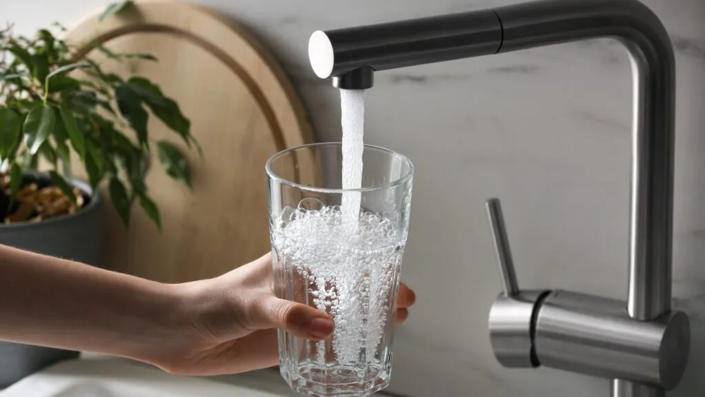 Woman filling glass with tap water from faucet in kitchen.