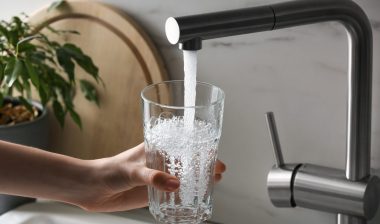 Woman filling glass with tap water from faucet in kitchen.