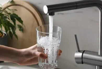 Woman filling glass with tap water from faucet in kitchen.