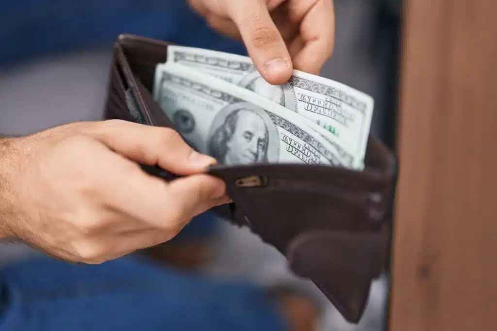 Close up of man holding his wallet with cash inside, representing recent class action rebates.
