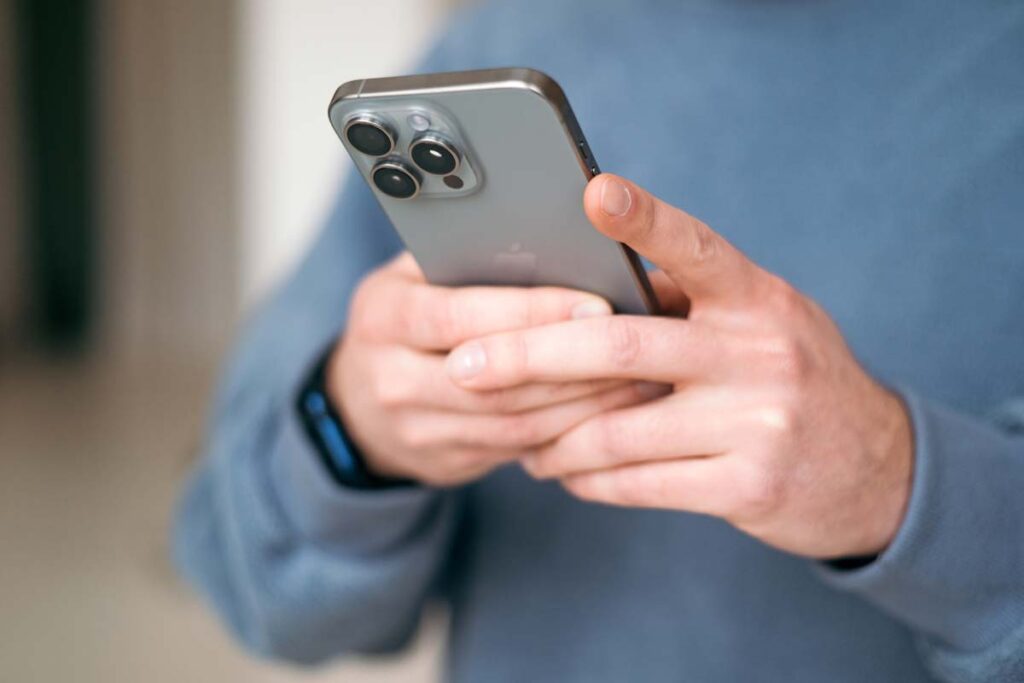 Close up of a man texting on an iPhone, representing two recent Apple iPhone antitrust class actions.