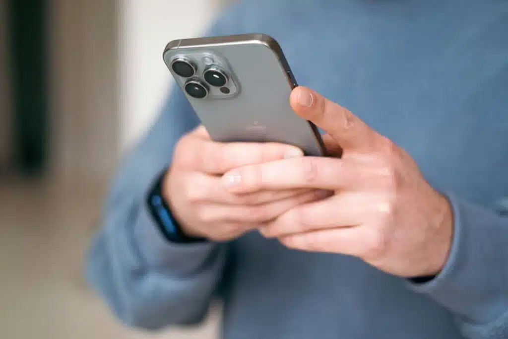 Close up of a man texting on an iPhone, representing two recent Apple iPhone antitrust class actions.