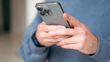 Close up of a man texting on an iPhone, representing two recent Apple iPhone antitrust class actions.