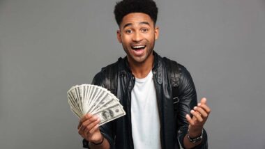 An excited man holding U.S. cash, representing recent settlement payments in the mail.