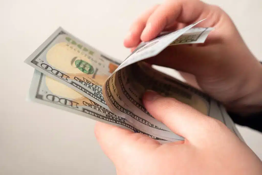 Close up of hands counting U.S. cash, representing recent class action rebates.