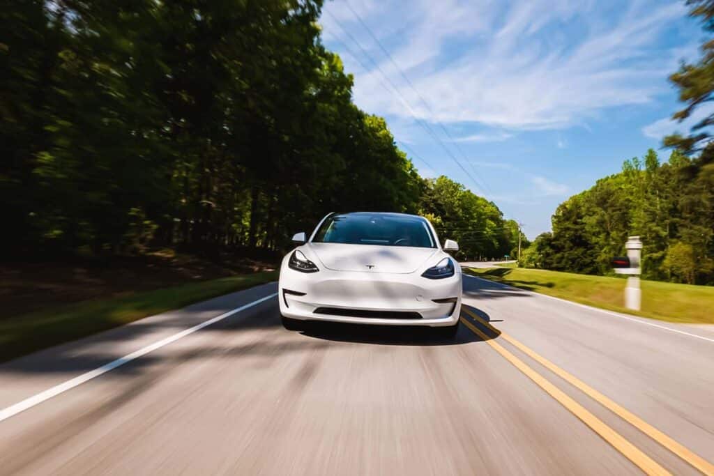 Front view of a white Tesla driving along a road, representing the Tesla Autopilot recall investigation.