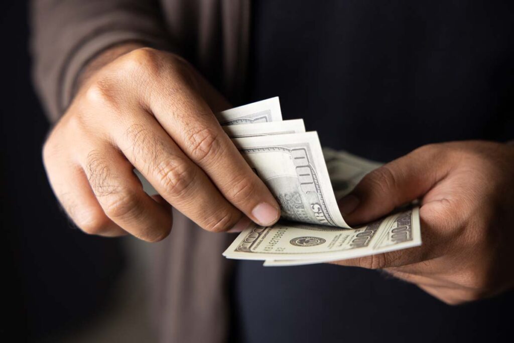 Close up of a mans hands counting U.S. cash, representing FTC refunds in April 2024.