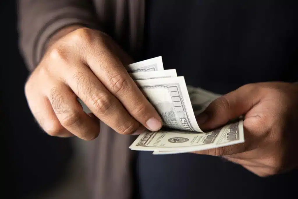 Close up of a mans hands counting U.S. cash, representing FTC refunds in April 2024.