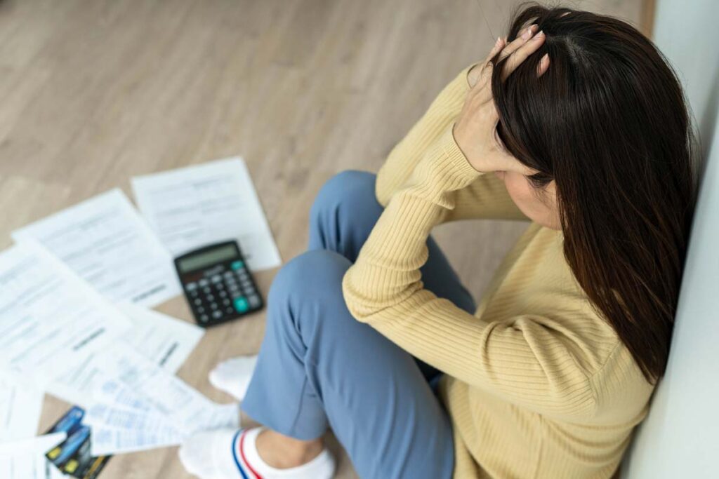 A stressed woman looking at her bills scattered on the floor, representing the Bradford Manor tenant settlement.