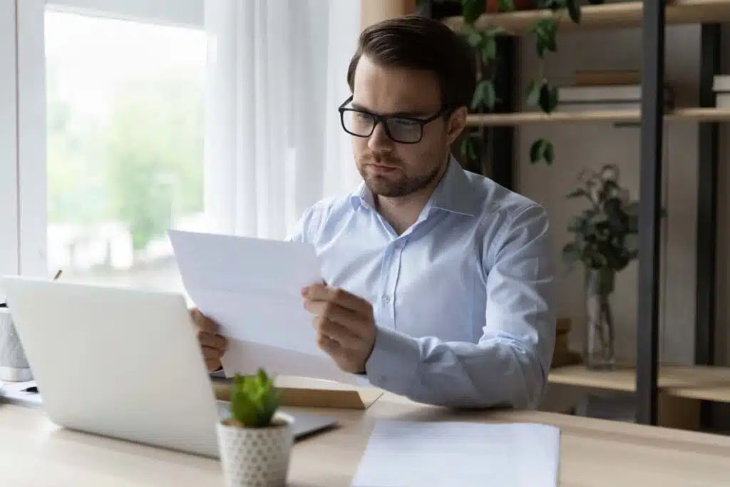 A serious man reading a letter from his mail, representing the Ocwen home loan fees settlement.