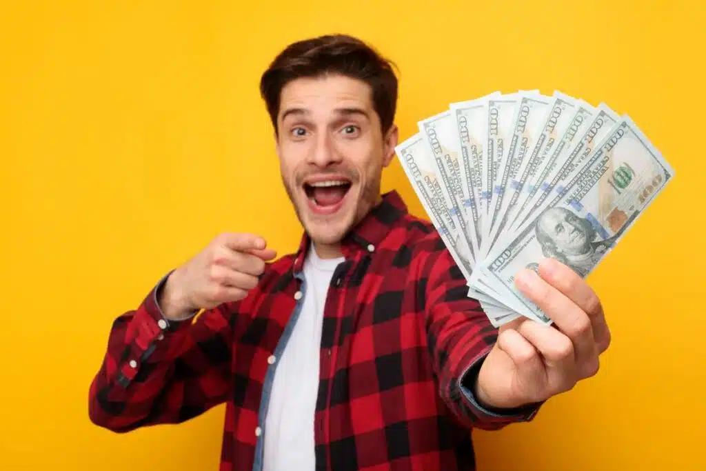 An excited man holding U.S. cash, representing recent settlement checks in the mail.