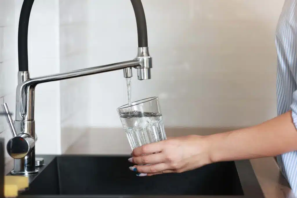 Close up of a woman filling a glass with water from a faucet, representing the drinking water contamination class action.