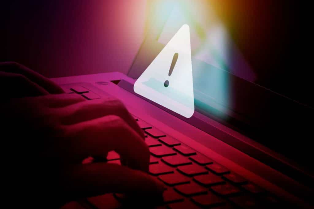 Close up of hands typing on a keyboard with a warning symbol overlay, representing the Ascension Health data breach class action.