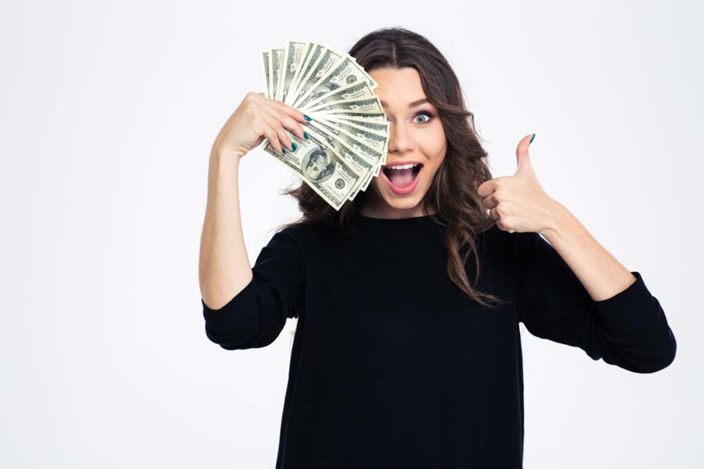 An excited woman holding cash and giving a thumbs up, representing checks in the mail in April.