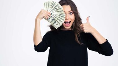 An excited woman holding cash and giving a thumbs up, representing checks in the mail in April.