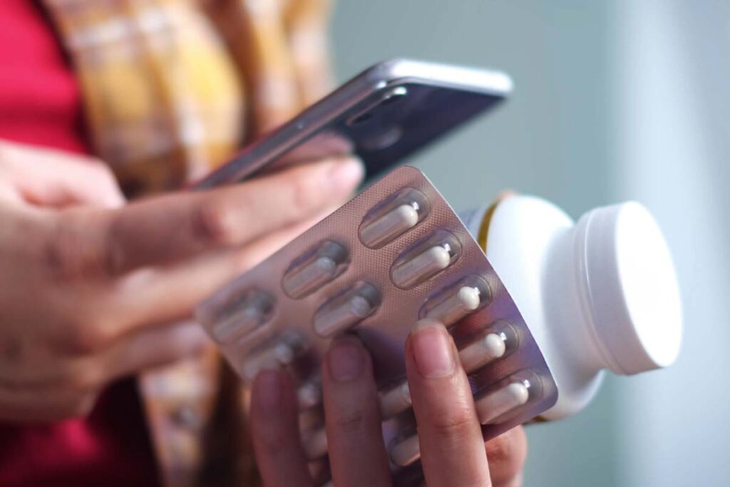 Close up of a woman holding pills and using her smartphone to order medicine, representing the Done Global Adderall arrests.