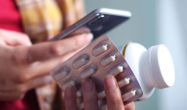 Close up of a woman holding pills and using her smartphone to order medicine, representing the Done Global Adderall arrests.