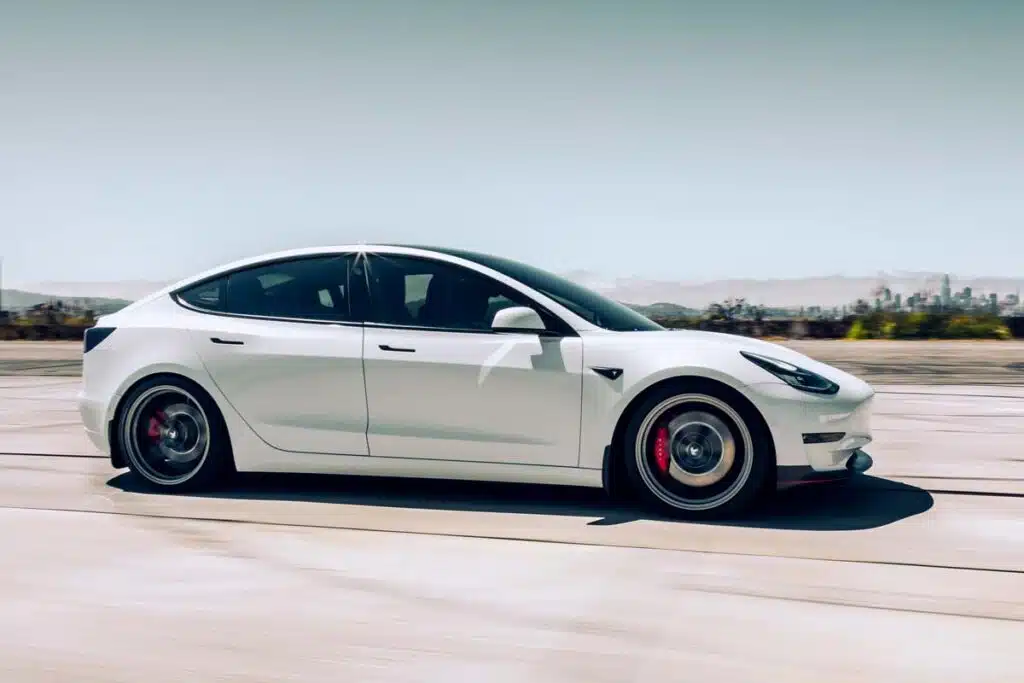 Side view of a white Tesla Model Y driving down a hgihway, representing the Tesla recall.