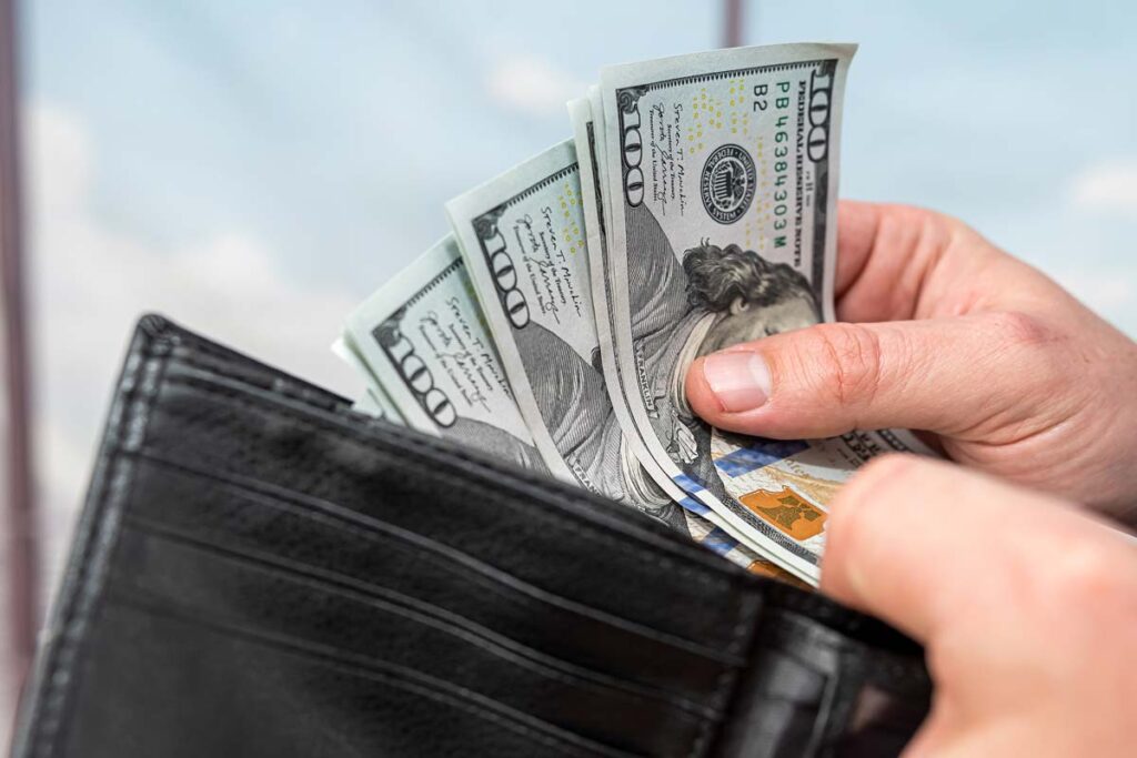 Close up of a man putting cash in a wallet, representing recent class action rebates.