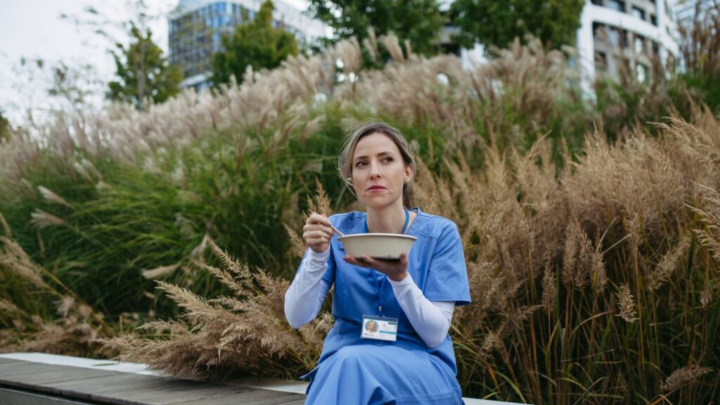 Nurse having healthy lunch, snack in front of hospital building, taking break from work.