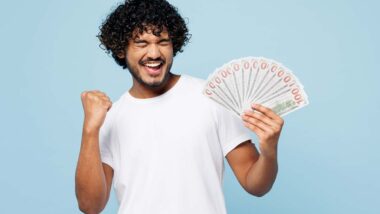 An excited man holding U.S. cash, representing recent settlement checks in the mail.