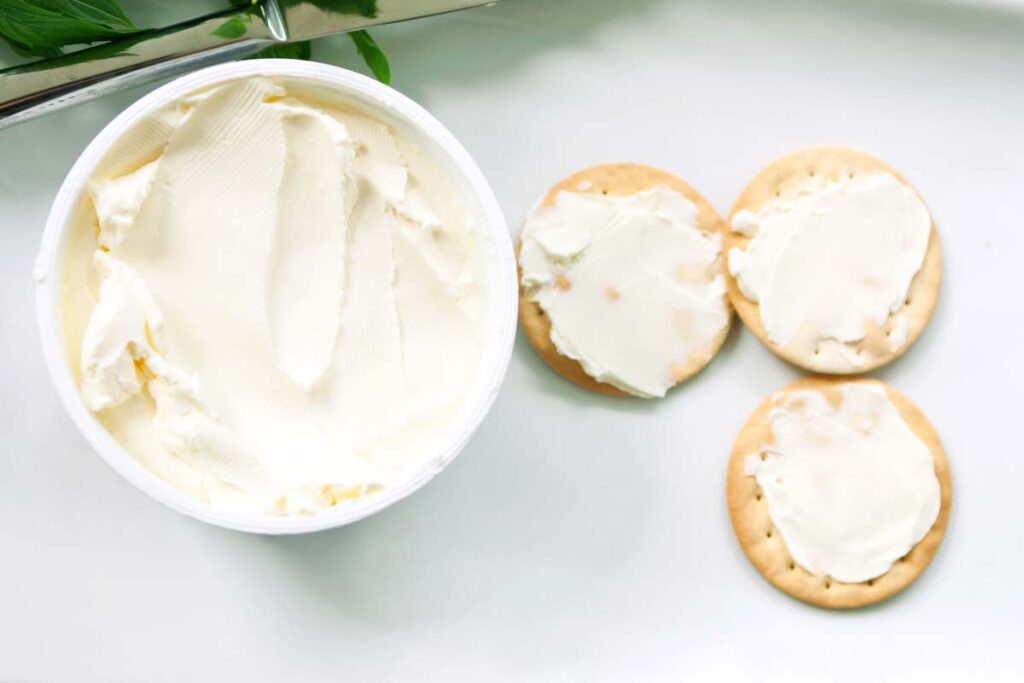 Cream cheese tub next to crackers with cream cheese, representing the cream cheese recall.