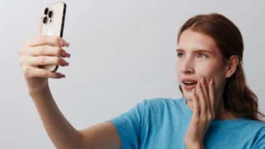 Dermatology app, young woman with clean skin holds smartphone for selfie